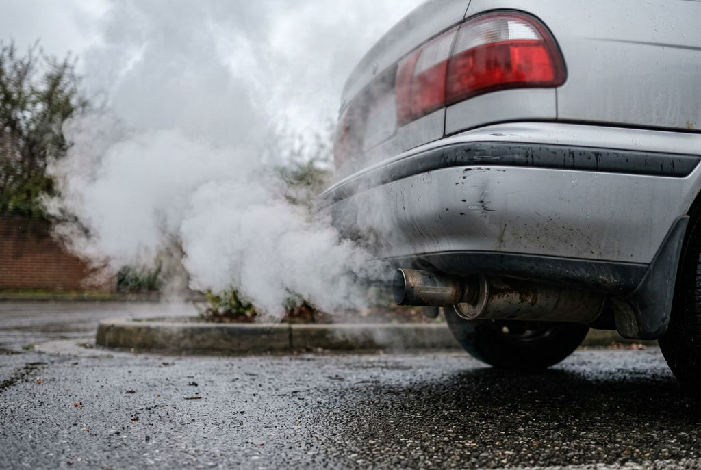 Dikke witte rook uit de uitlaat van een auto, een teken van koelvloeistof in de verbrandingskamer door een lekke koppakking
